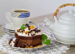 Na talerzyku ciasto czekoladowe z listkami mięty. W tle dzbanek i filizanka z kawą. Stylizacja kulinarna
